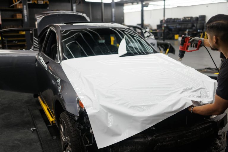 Car being wrapped with white vinyl in an auto workshop by a skilled mechanic.